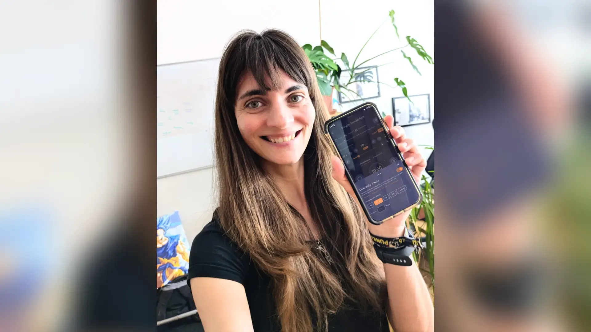 Verena Zaiser smiling and holding up a phone that shows the Drumbitious metronome with the Dynamic mode sheet open